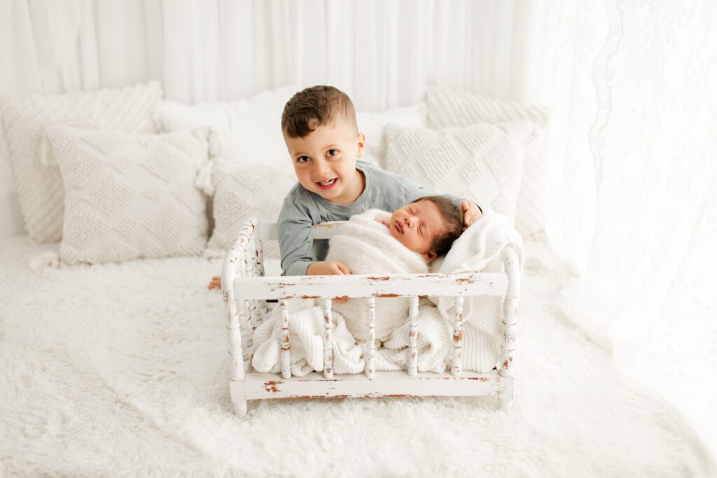 Little boy from Winnetka kneeling next to his baby brother as baby sleeps in a tiny crib